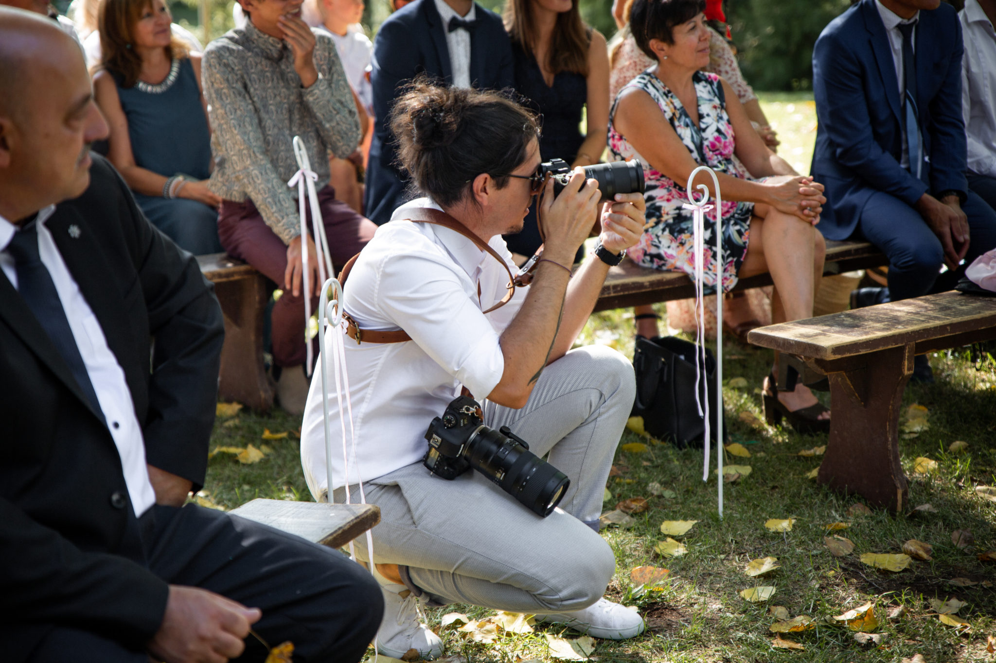 Portrait du photographe de mariage Aurélien Kirchner en train de photographier des mariés pendant la cérémonie laïque au milieu des invités