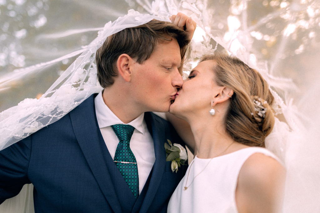 Portrait des mariés qui s'embrassent sous le voile de la mariée dans une lumière douce et chaleureuse.