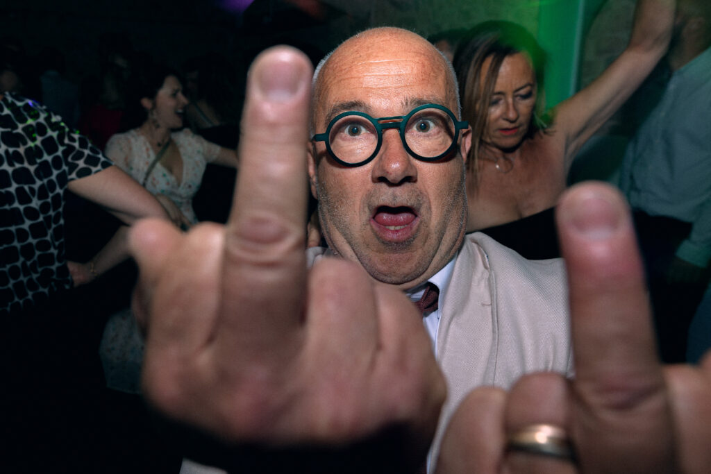 Le papa du marié me fait deux gros doigts d'honneur face à l'appareil photo pendant la soirée dansante.